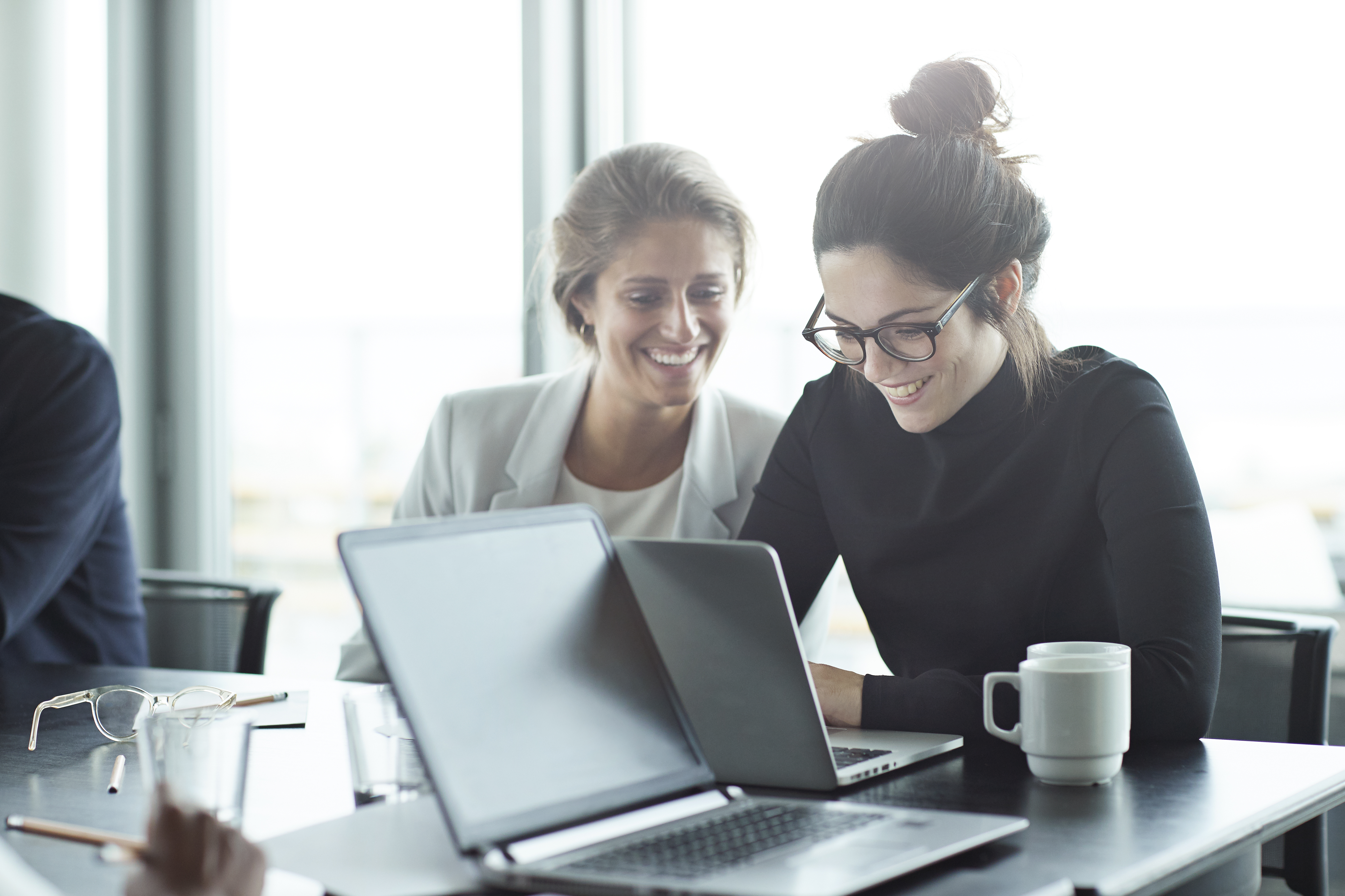 Two female co-workers in an office meeting sharing a laptop.
